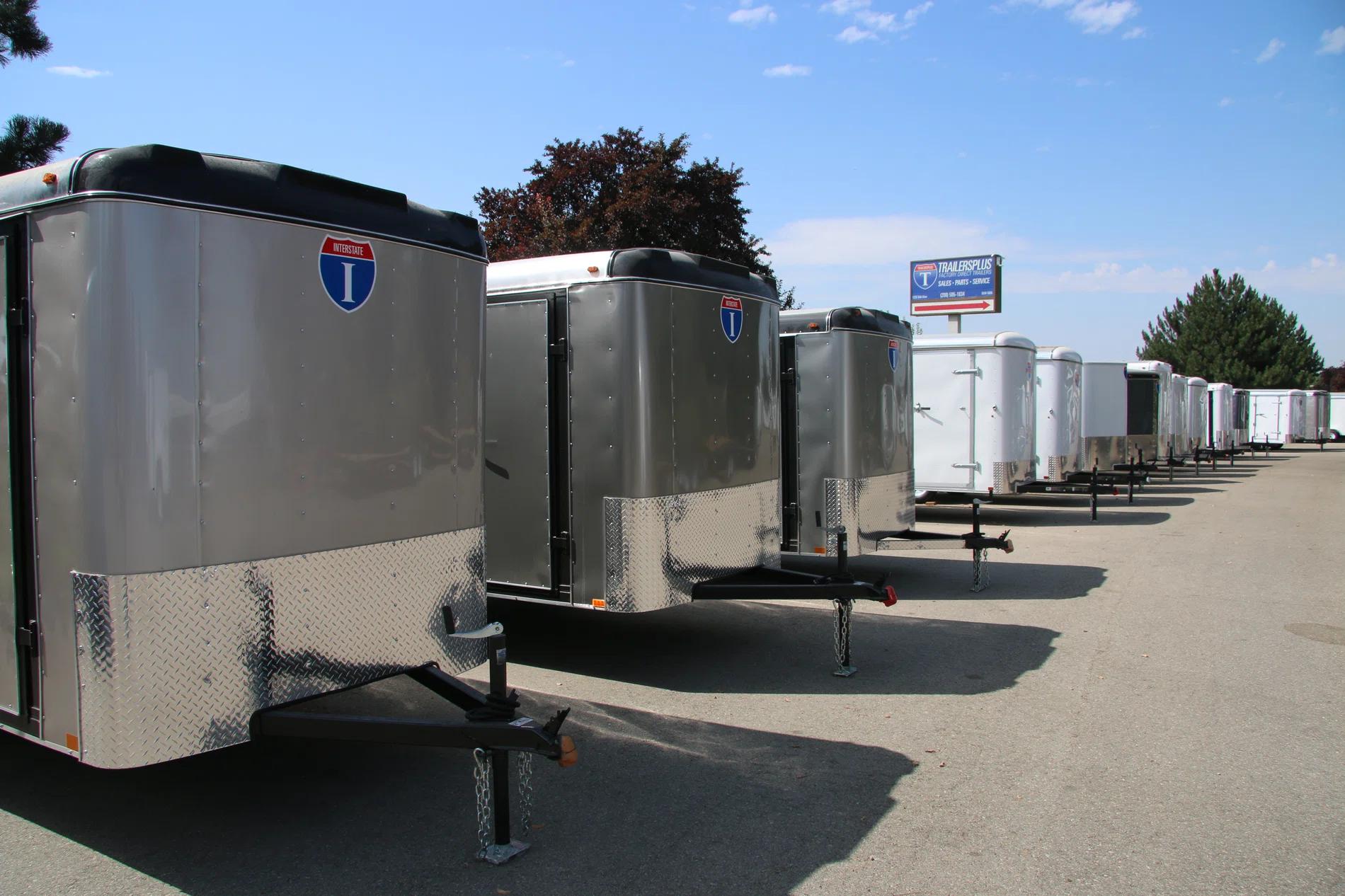 Receding row of silver Interstate enclosed cargo trailers parked angled at a sunny TrailersPlus dealer lot