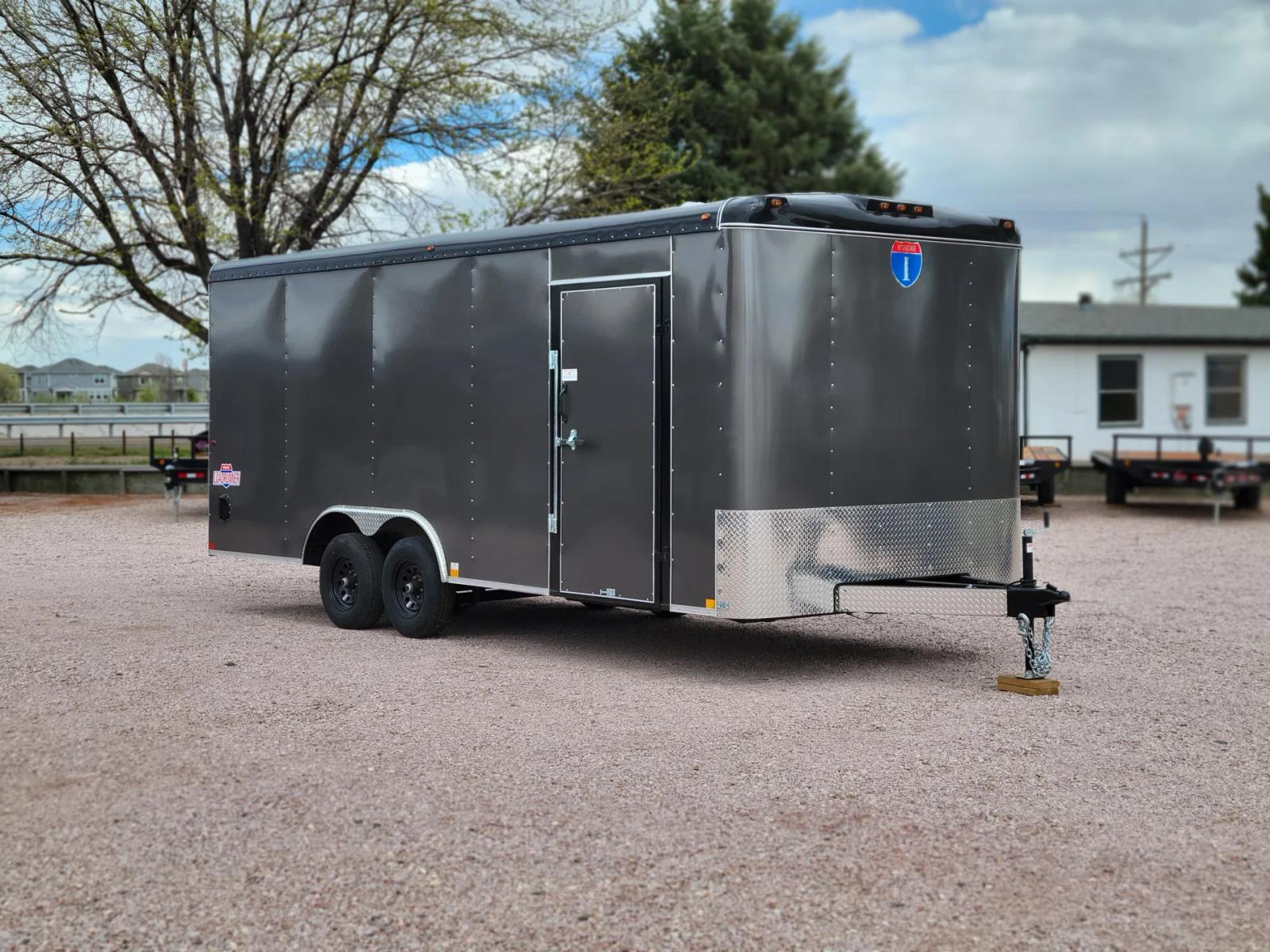 Black tandem-axle dump trailer with the bed tilted up at full dump angle on a sunny lot among rows of trailers