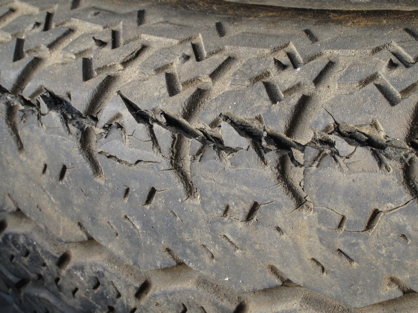 Close-up of a worn trailer tire tread with visible cracks and dry-rot damage along the rubber