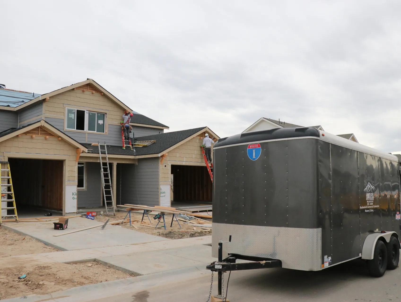 Charcoal Interstate enclosed cargo trailer parked at a residential framing site with workers on ladders at a two-story home