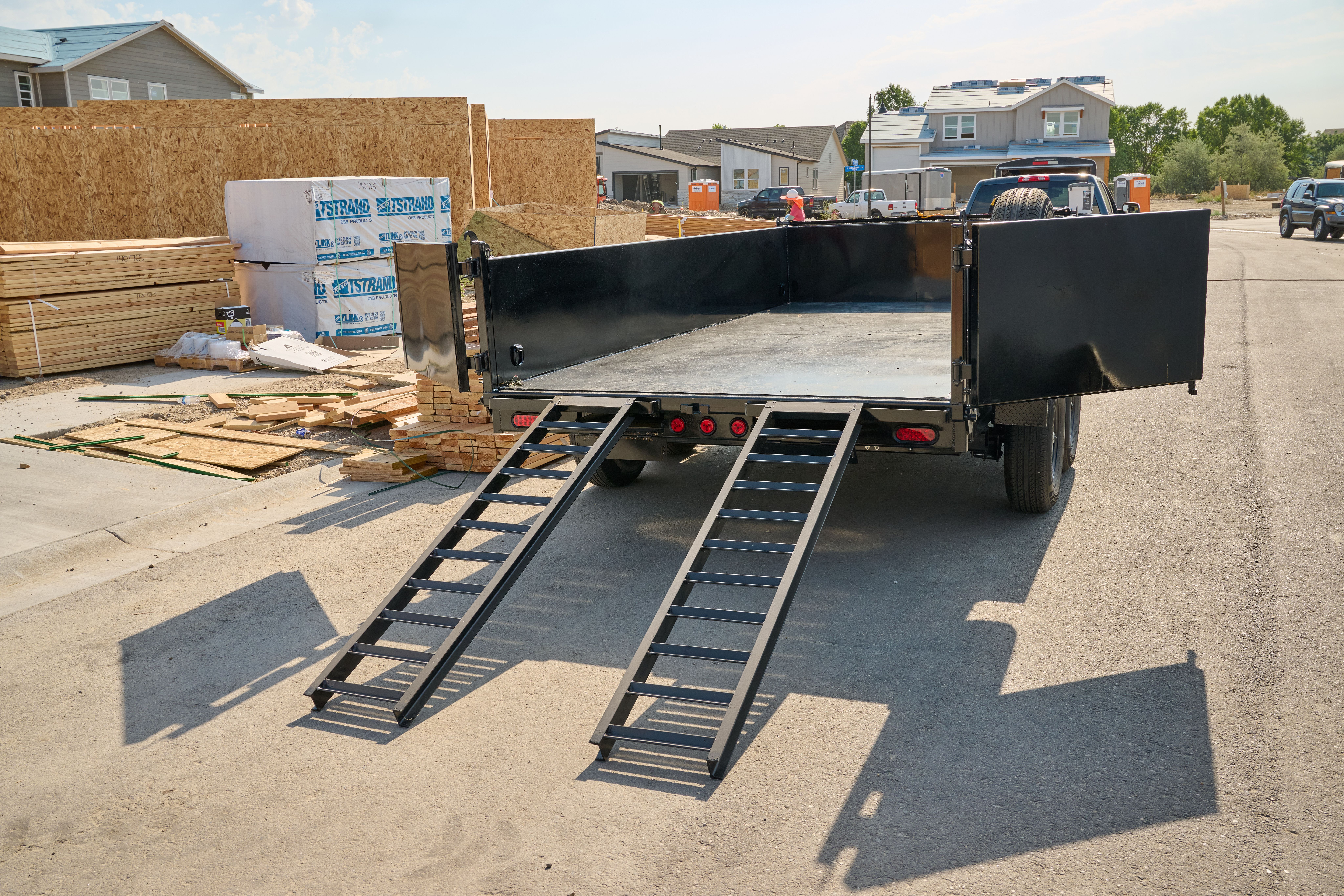 Rear view of a black dump trailer, with ramps down and doors open