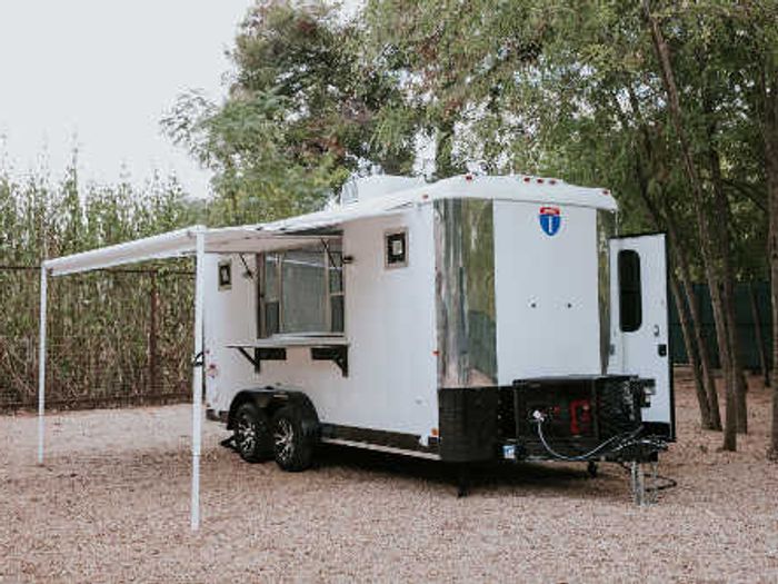 Group of attendees seated at picnic tables in front of a black TrailersPlus mobile event trailer at an outdoor tailgate gathering