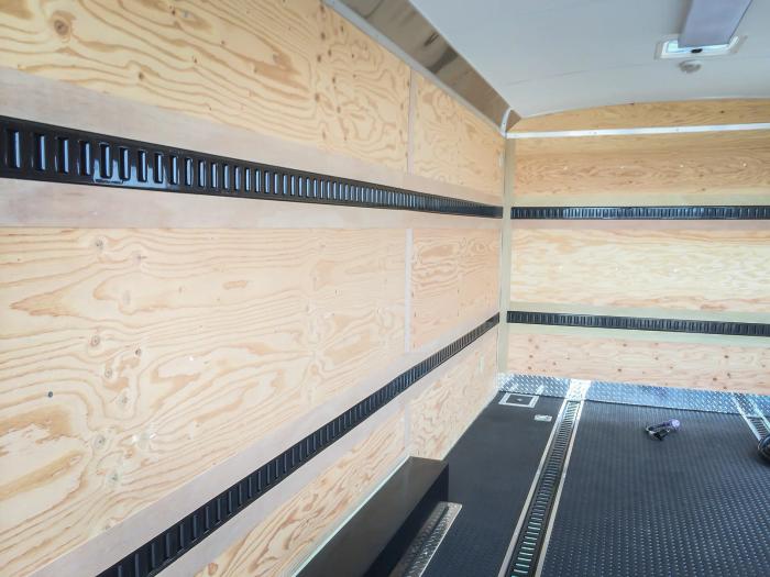 Interior of an enclosed cargo trailer with plywood walls, mounted black E-track tie-down rails, and a black TPO floor