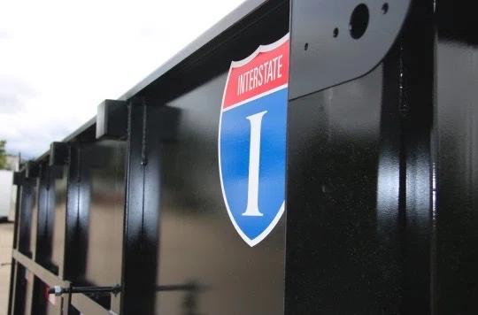 Close-up of a black trailer's side panel with a red, white, and blue Interstate I-shield decal