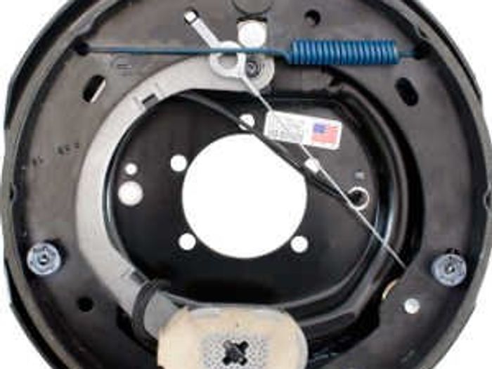 Close-up of an exploded trailer drum-brake assembly showing the backing plate, springs, and brake lines