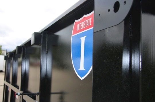 Close-up of a black trailer's side panel with a red, white, and blue Interstate I-shield decal