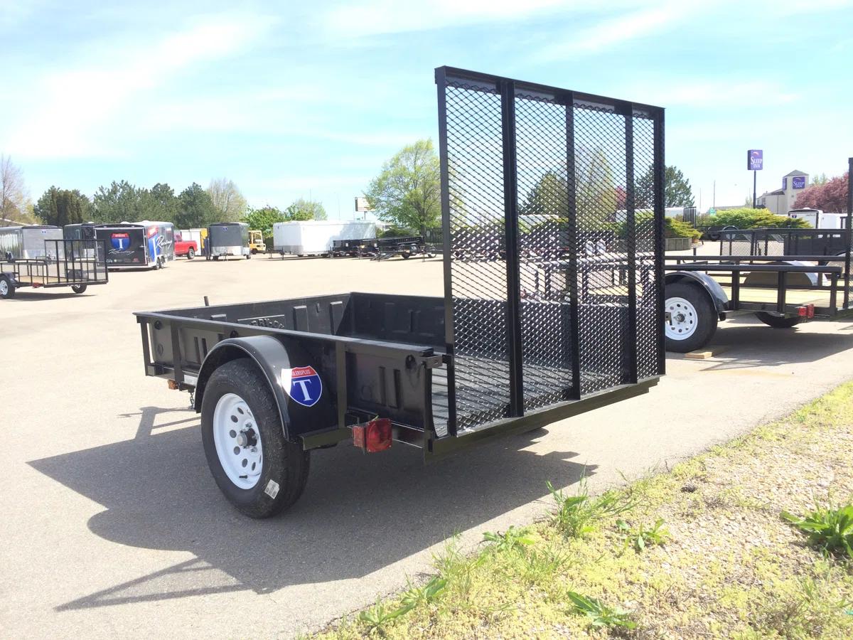 Three white enclosed cargo trailers parked at angled spaces under tall shade trees in a paved lot
