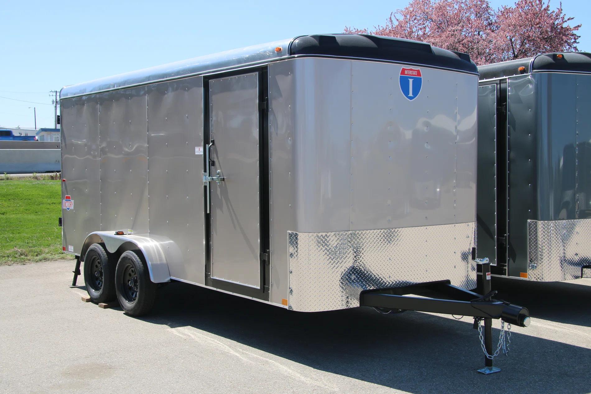 Person crouched inside the plywood-lined interior of an enclosed cargo trailer with rear doors open at a workshop