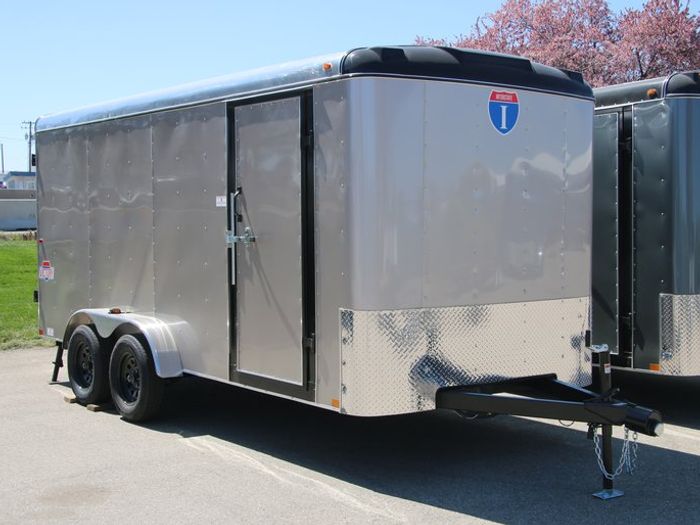 Rows of black single-axle utility trailers with wood decks lined up at a sunny TrailersPlus dealer lot