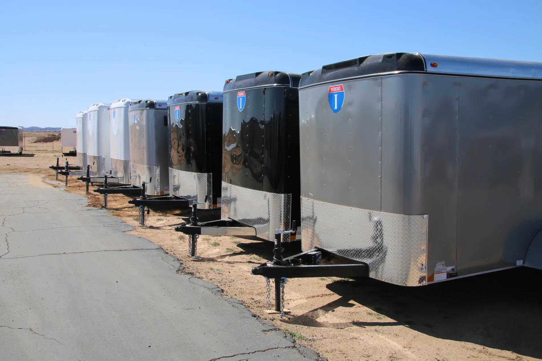 Row of small silver Interstate enclosed cargo trailers angled in line at a sunny TrailersPlus dealer lot