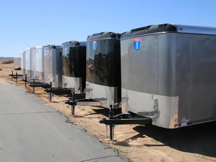 Row of small silver Interstate enclosed cargo trailers angled in line at a sunny TrailersPlus dealer lot