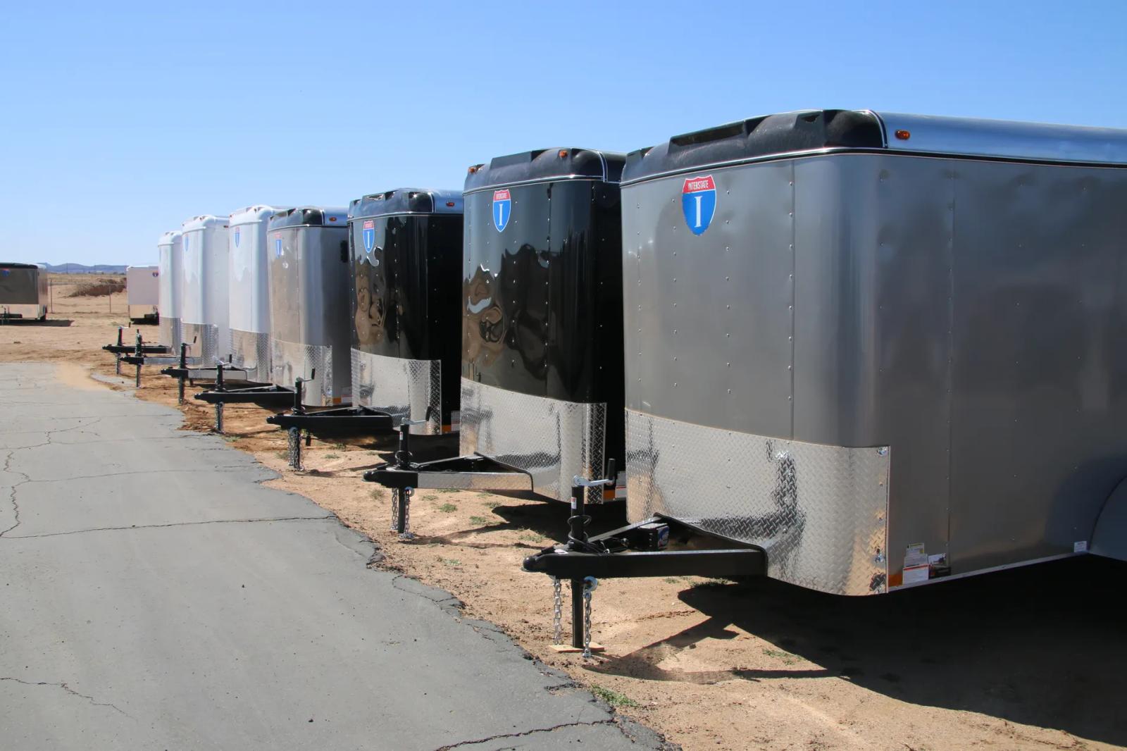 Row of small silver Interstate enclosed cargo trailers angled in line at a sunny TrailersPlus dealer lot