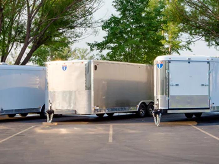 Three white enclosed cargo trailers parked at angled spaces in a tree-lined paved lot