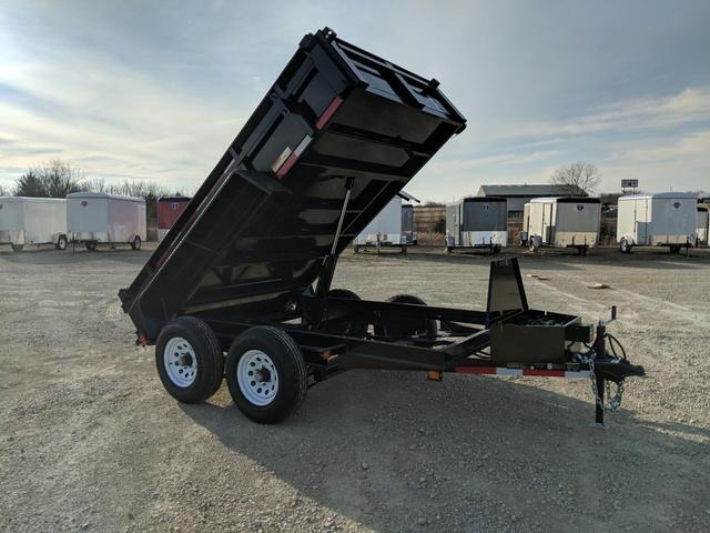 Three black dump trailers of varying sizes parked side-by-side on a sandy dealer lot under a clear sky