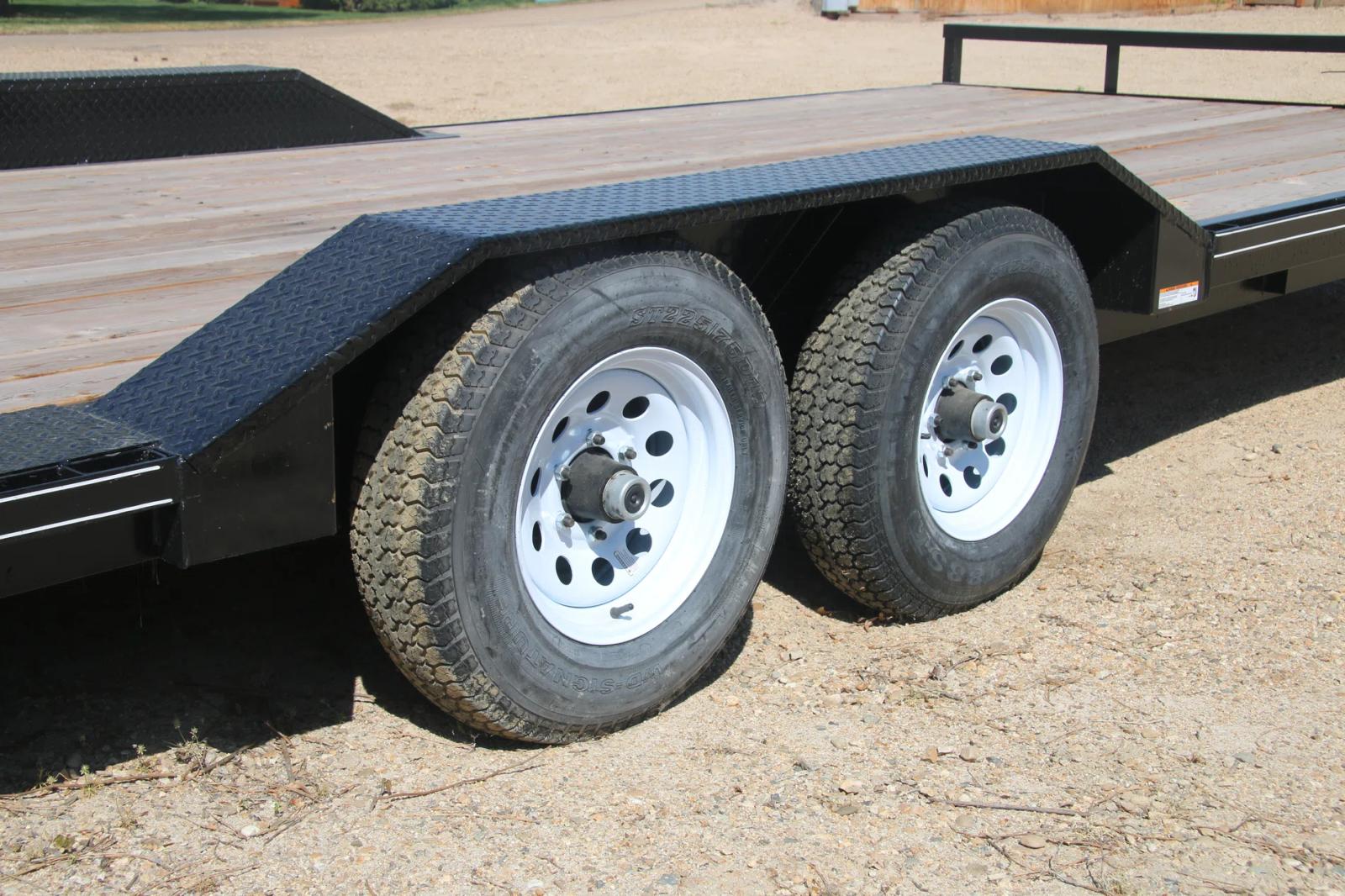 Close-up of a black equipment trailer's tandem axles with silver wheels and the edge of its wood plank deck