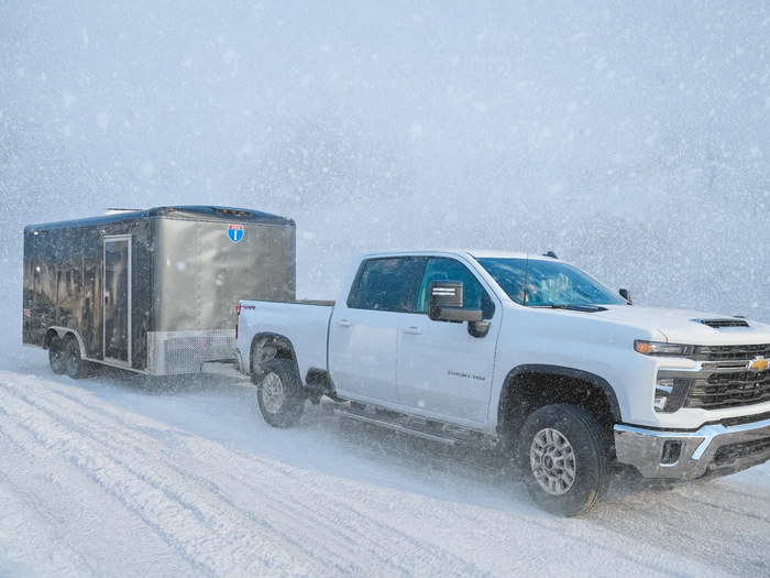 Gray cargo trailer in a snowstorm, with a white chevrolet truck