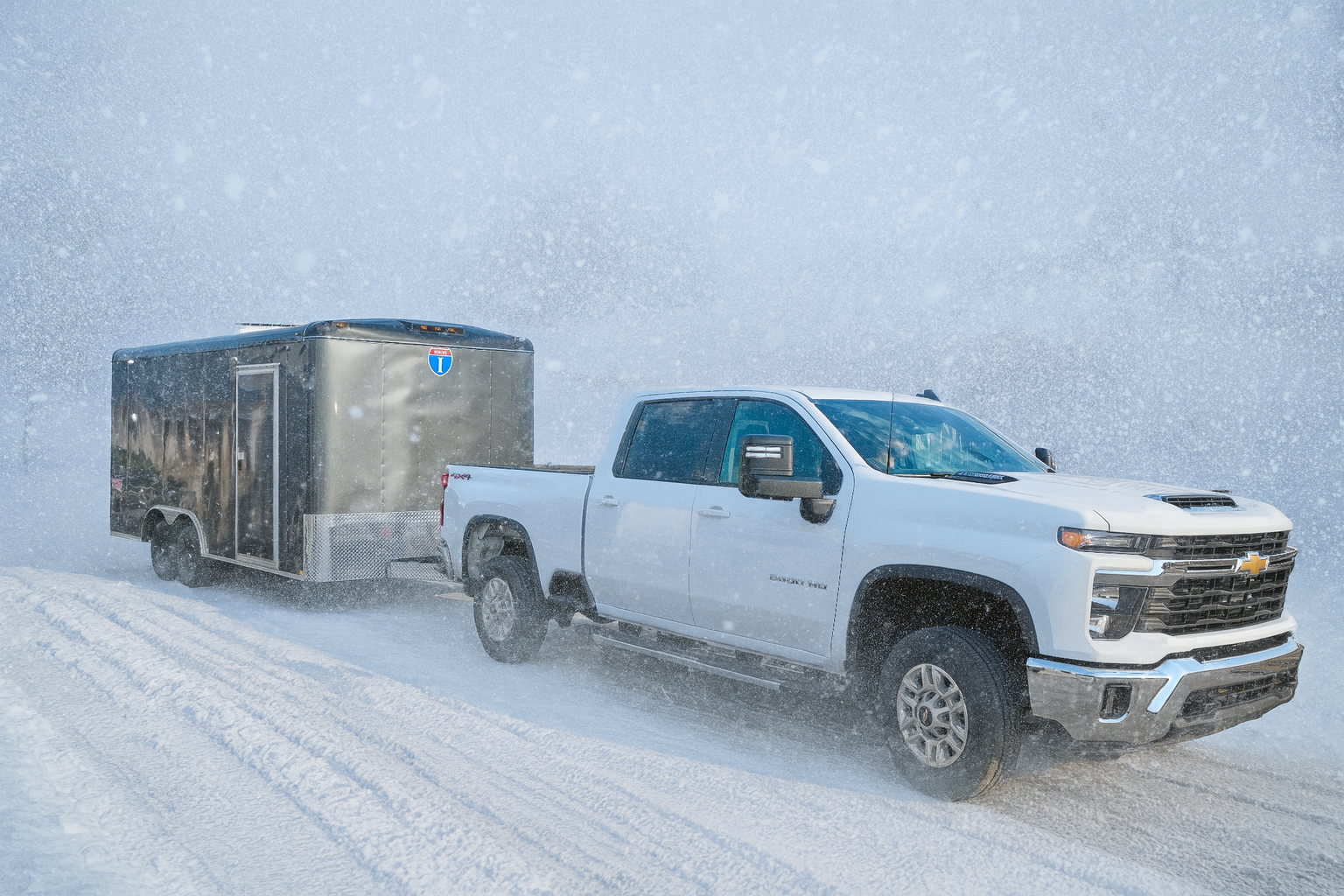 Gray cargo trailer in a snowstorm, with a white chevrolet truck