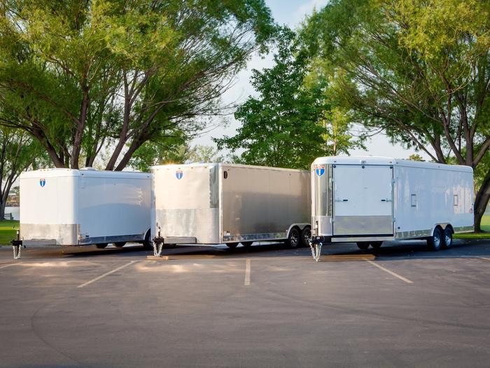 Silver-gray Interstate enclosed cargo trailer parked on asphalt under a flowering tree on a sunny day