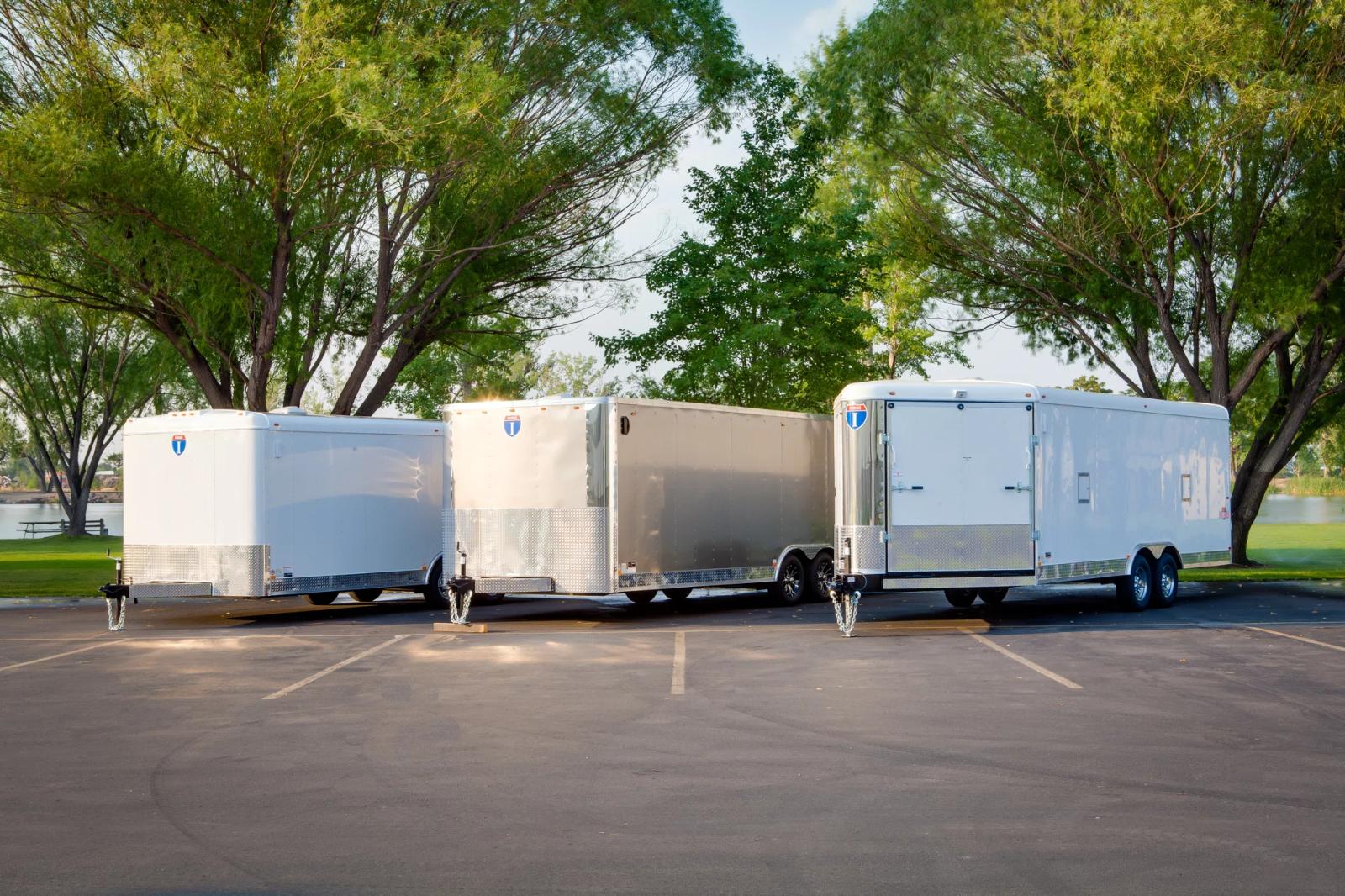 Silver-gray Interstate enclosed cargo trailer parked on asphalt under a flowering tree on a sunny day