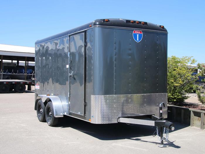 Lineup of a black utility trailer, flatbed deckover, gooseneck dump, and enclosed cargo trailers parked together on a TrailersPlus dealer lot under cloudy skies