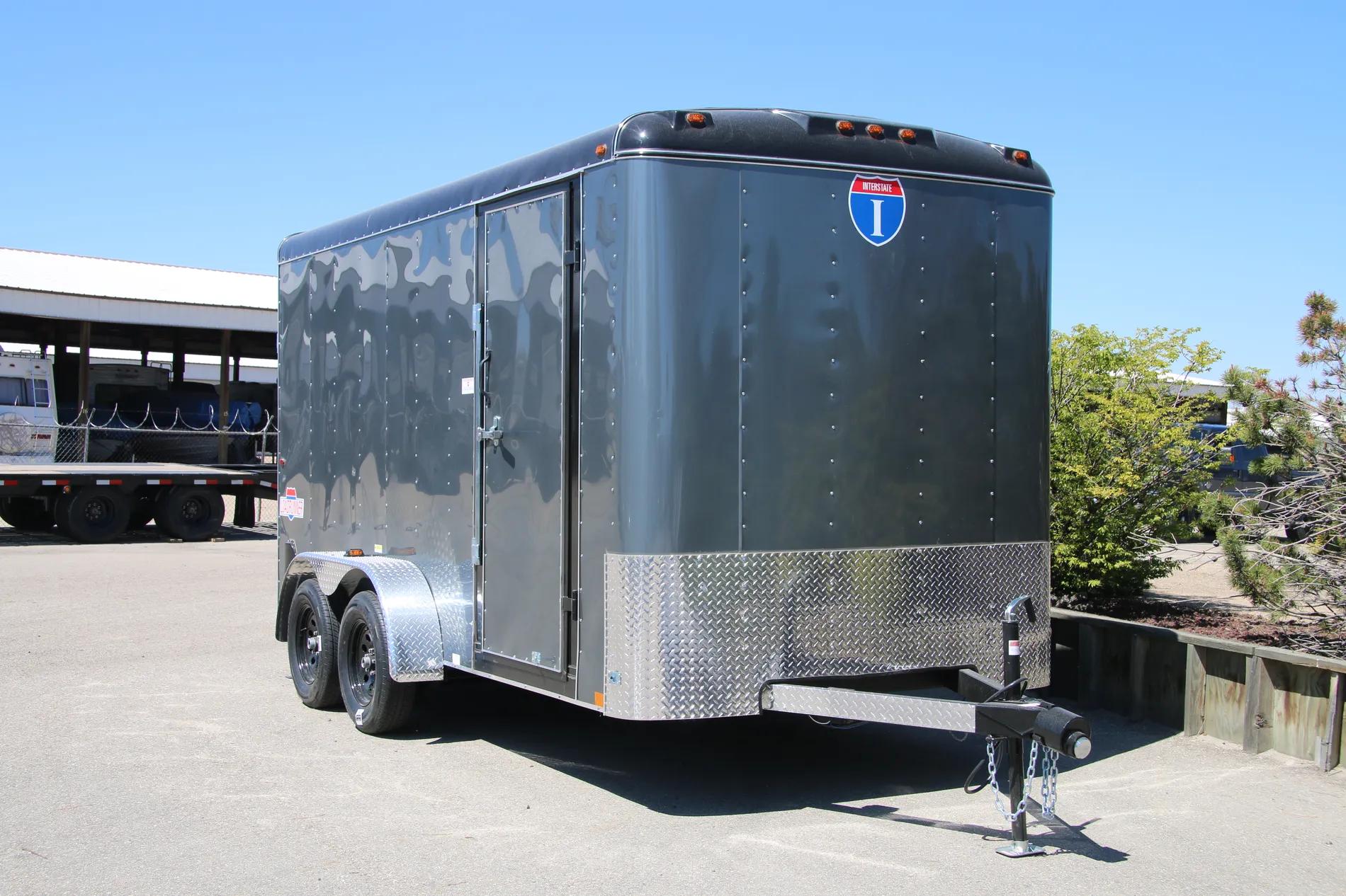 Charcoal-gray Interstate enclosed cargo trailer with diamond-plate stone guard parked on asphalt under a clear blue sky