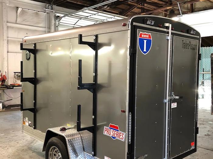 Silver Interstate Pro Series enclosed cargo trailer with three exterior ladder racks mounted on the side in a workshop