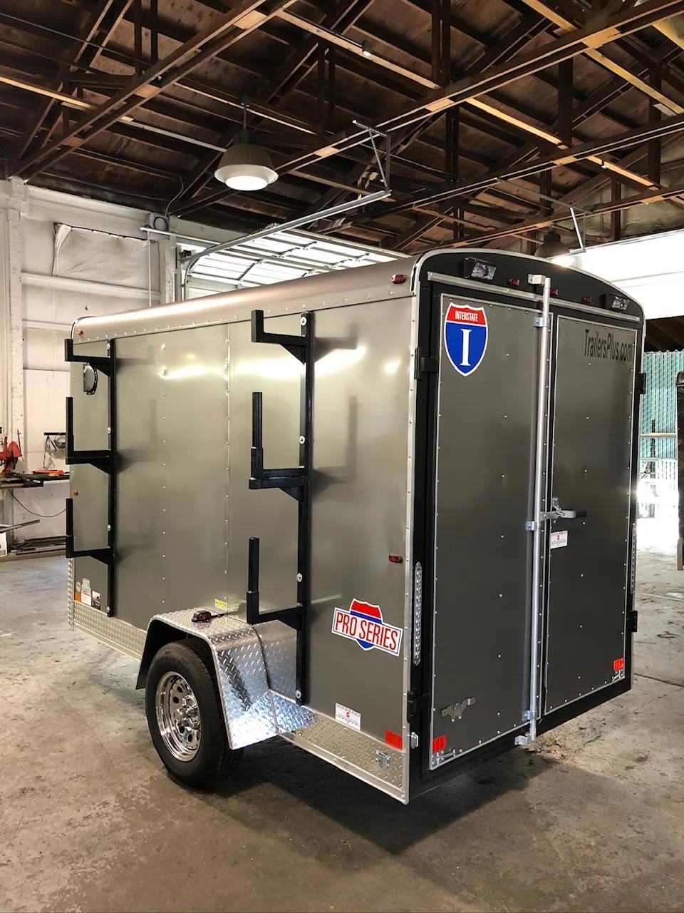 Silver Interstate Pro Series enclosed cargo trailer with three exterior ladder racks mounted on the side in a workshop