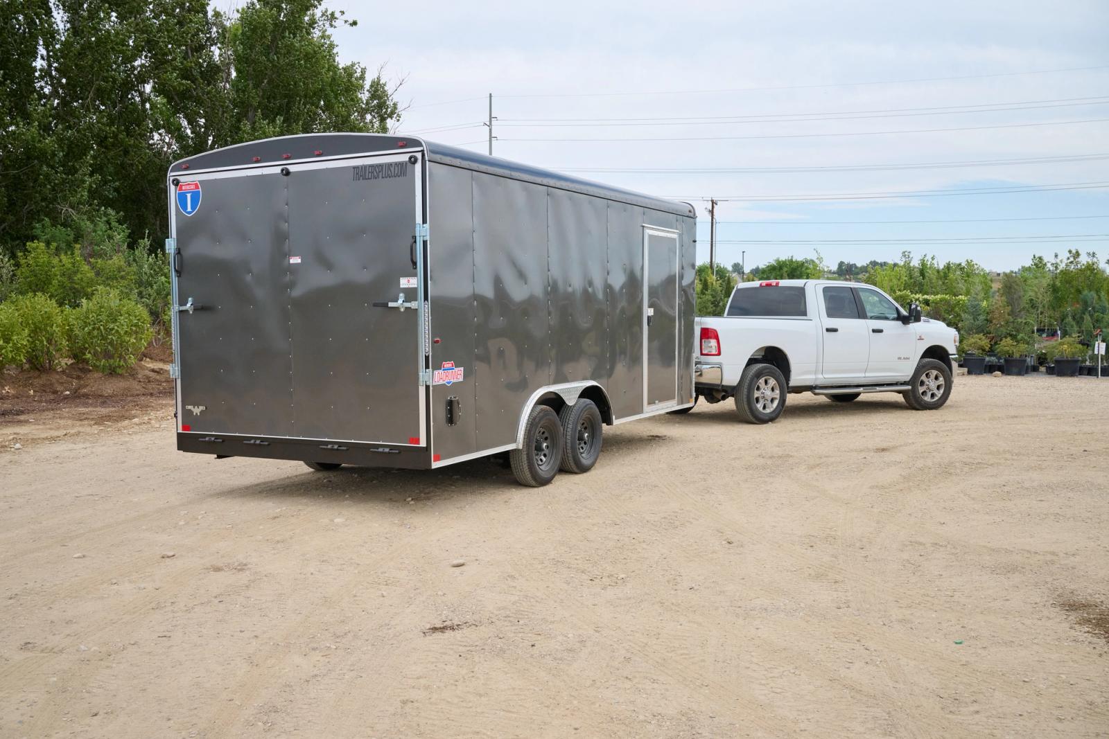 Rear view of gray enclosed cargo trailer attached to white dodge truck