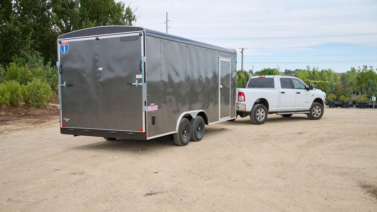 Rear view of gray enclosed cargo trailer attached to white dodge truck