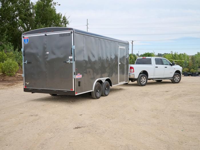 Rear view of gray enclosed cargo trailer attached to white dodge truck