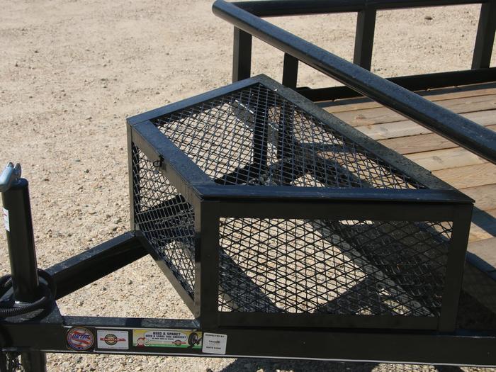 Close-up of a wire-mesh tongue storage box mounted to the front rail of a black utility trailer