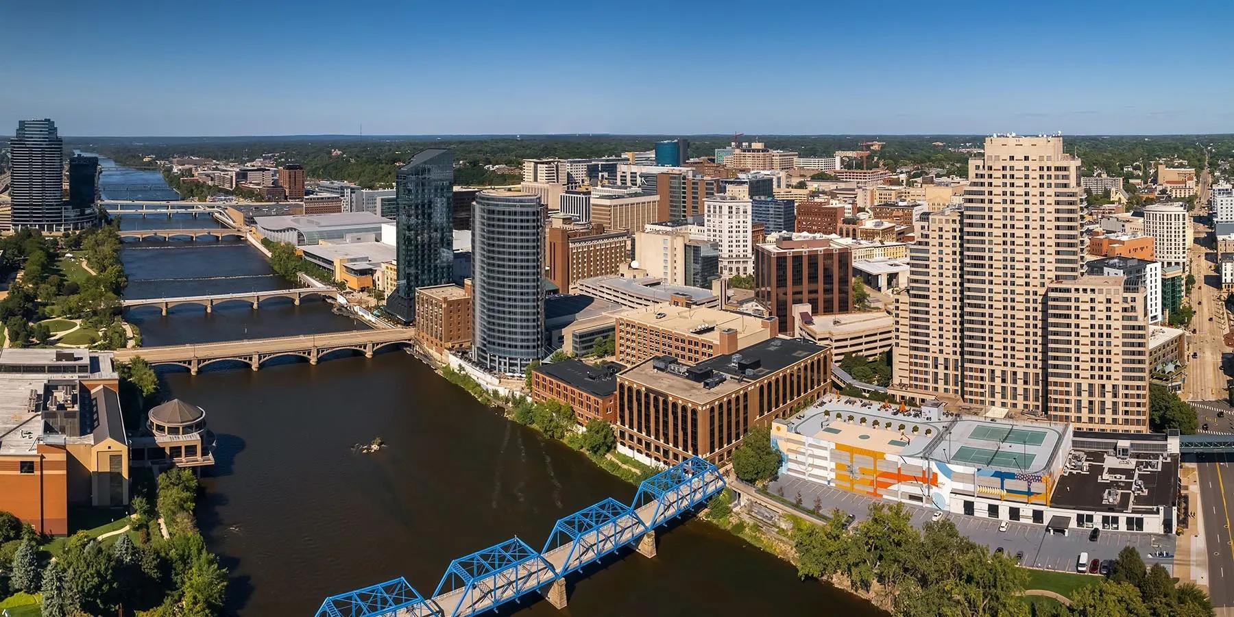Aerial view of downtown Grand Rapids, Michigan with the blue truss pedestrian bridge spanning the river and mid-rise buildings beyond