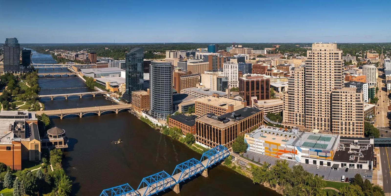 Aerial view of downtown Grand Rapids, Michigan with the blue truss pedestrian bridge spanning the river and mid-rise buildings beyond