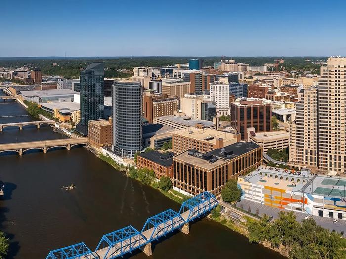 Aerial view of downtown Grand Rapids, Michigan with the blue truss pedestrian bridge spanning the river and mid-rise buildings beyond