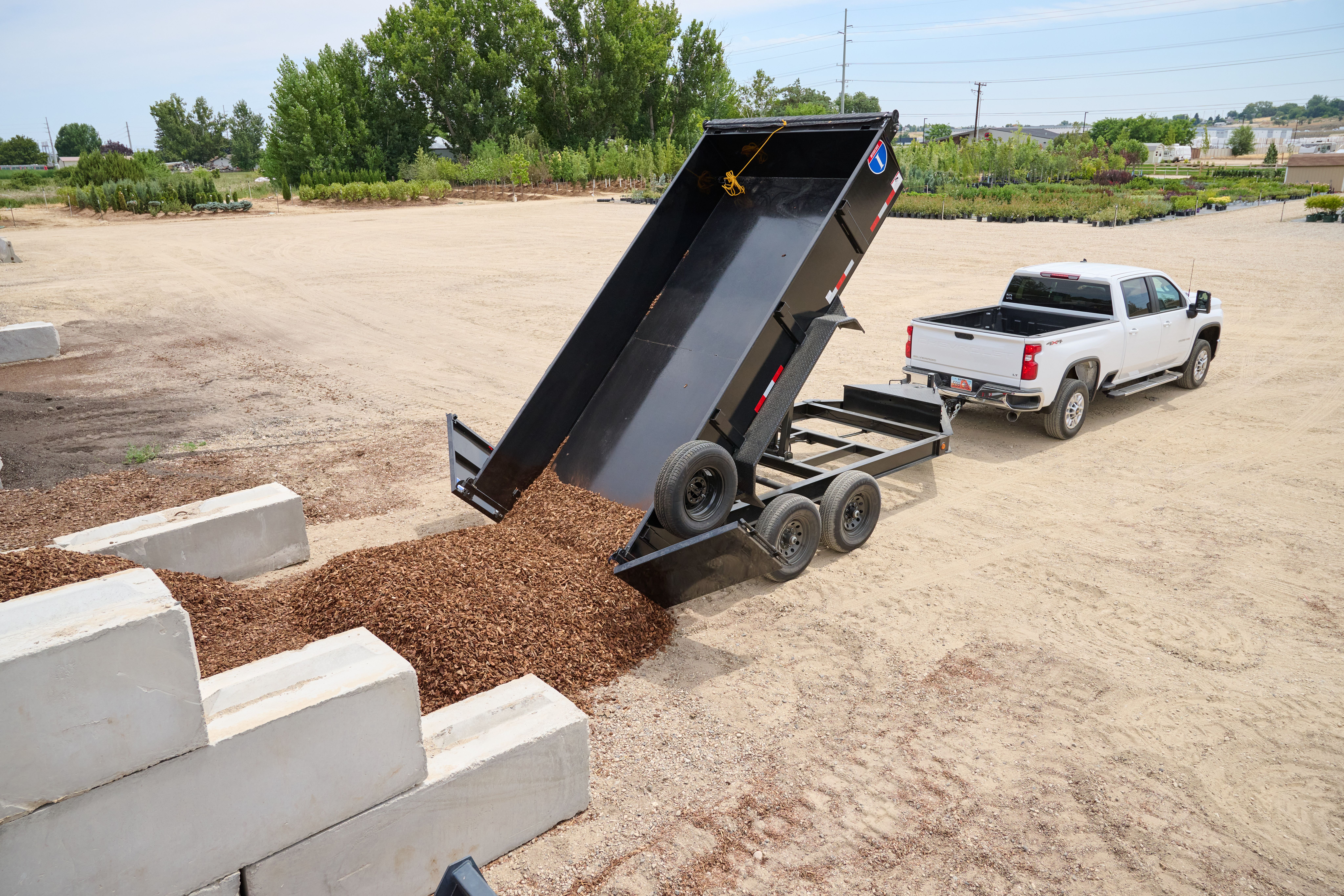 Dump trailer dumping mulch attached to a white chevrolet truck