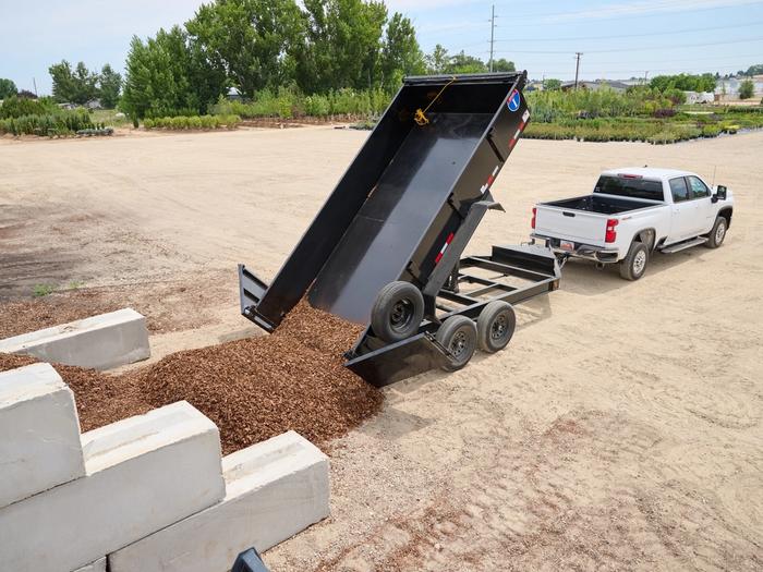 Dump trailer dumping mulch attached to a white chevrolet truck
