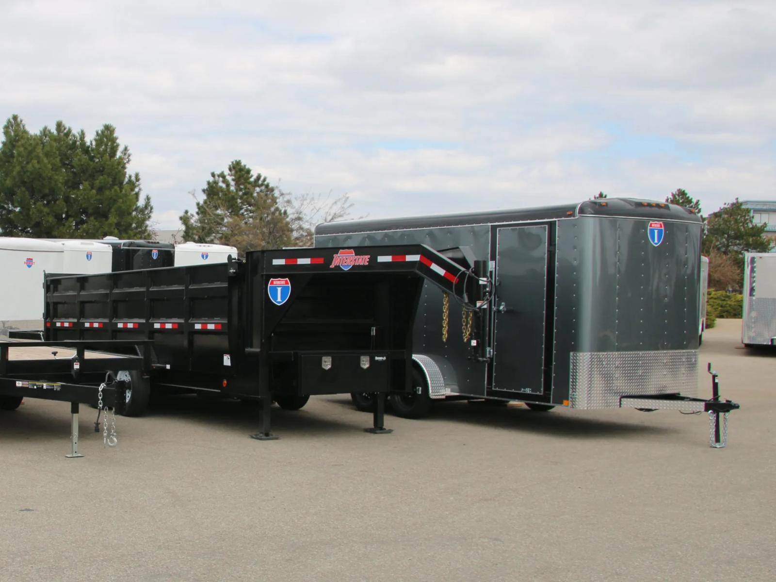 Black Interstate gooseneck dump trailer parked alongside a charcoal Interstate enclosed cargo trailer at a TrailersPlus dealer lot