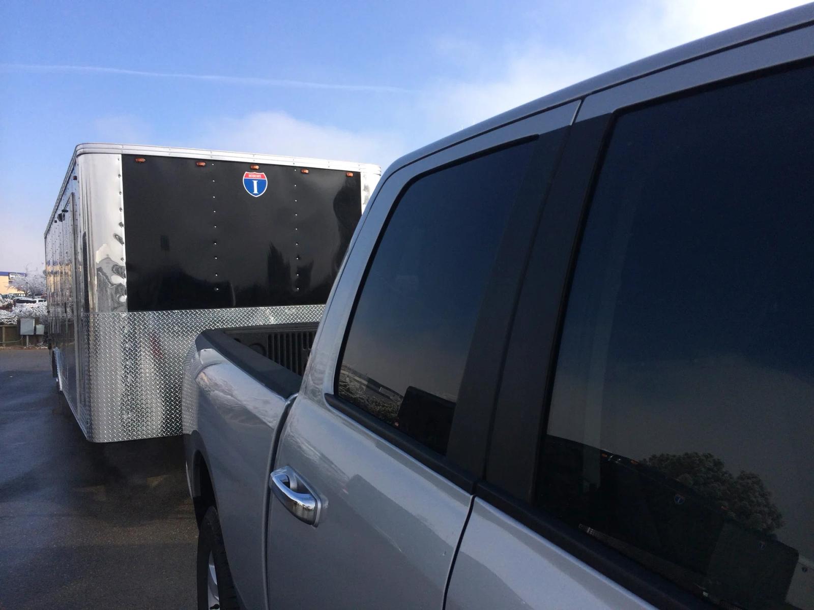 Silver pickup truck parked alongside a black-and-silver Interstate enclosed cargo trailer at a sunny dealer lot
