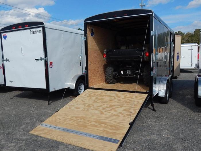 White Patriot-brand enclosed cargo trailer with side door and tandem axles parked on asphalt beside a grassy roadside