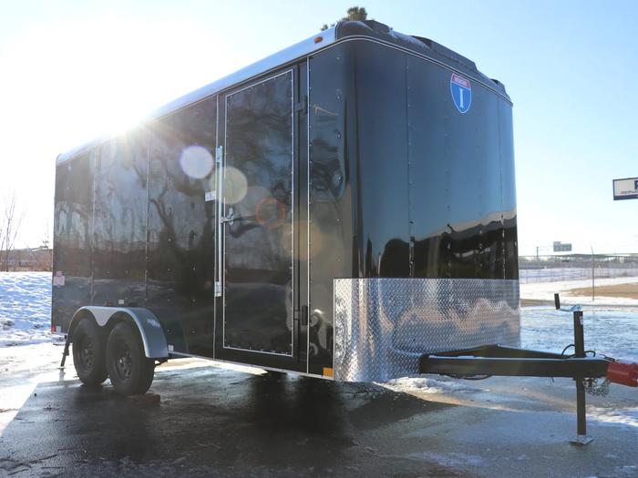 Black Interstate enclosed cargo trailer with diamond-plate guard parked on a sunlit icy asphalt lot with patches of snow