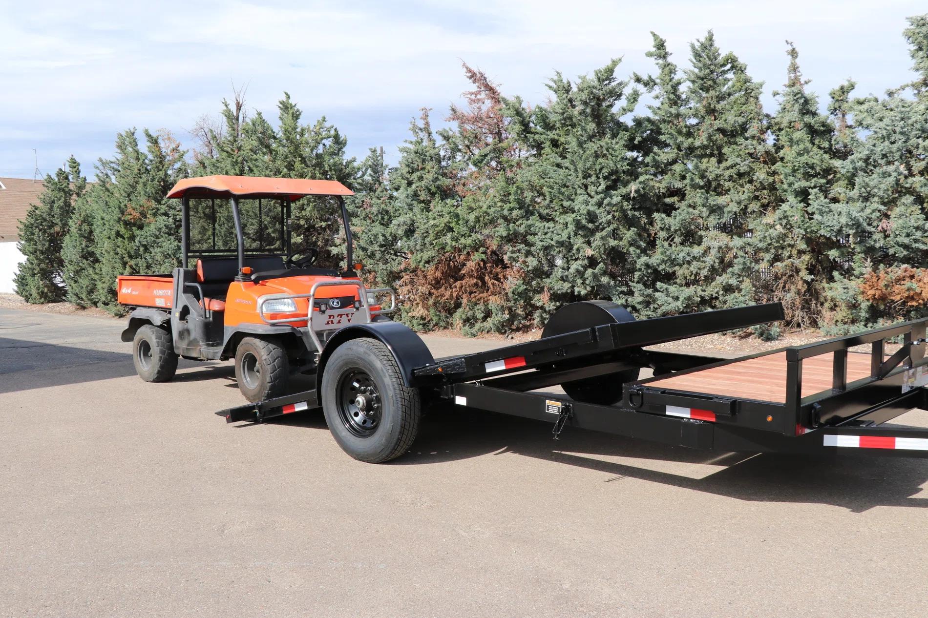 Orange Kubota RTV utility vehicle parked beside a black single-axle tilt equipment trailer with wood deck