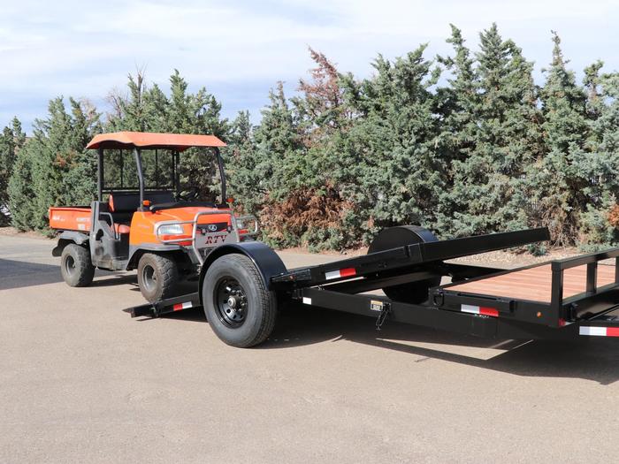 Orange Kubota RTV utility vehicle parked beside a black single-axle tilt equipment trailer with wood deck