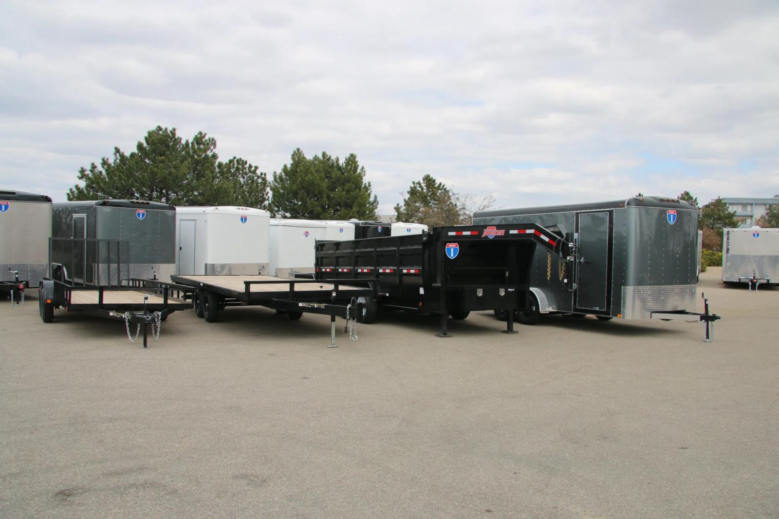 Lineup of a black utility trailer, flatbed deckover, gooseneck dump, and enclosed cargo trailers parked together on a TrailersPlus dealer lot under cloudy skies