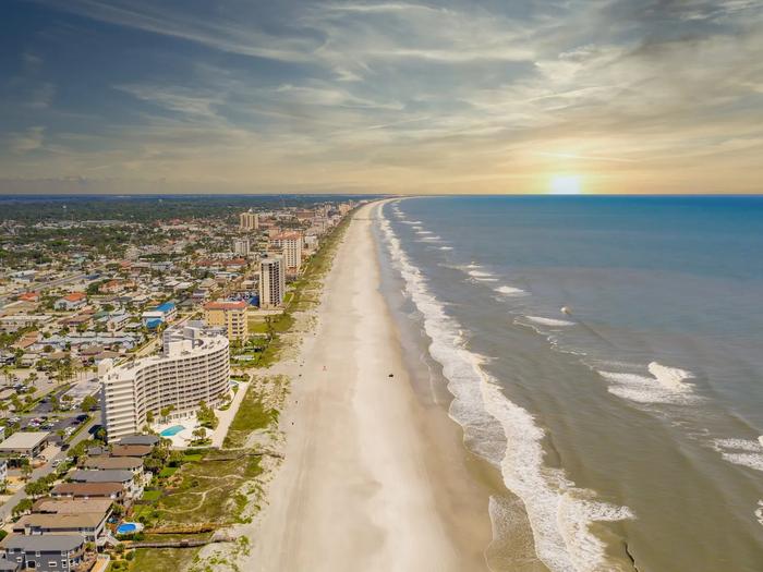 Aerial view of Jacksonville's beachfront with high-rise condos along white sand and the Atlantic Ocean at sunset