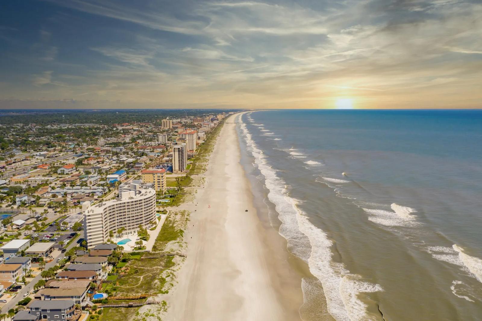Aerial view of Jacksonville's beachfront with high-rise condos along white sand and the Atlantic Ocean at sunset