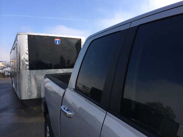 Silver pickup truck parked alongside a black-and-silver Interstate enclosed cargo trailer at a sunny dealer lot