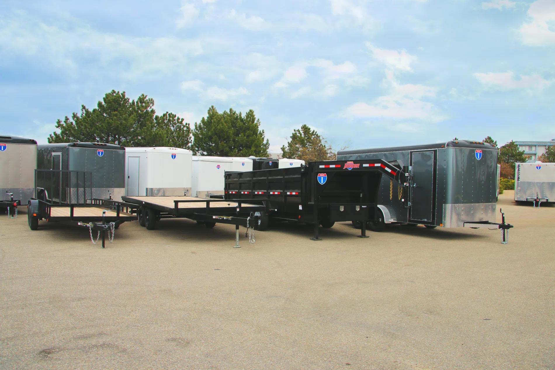 Lineup of a black utility, flatbed deckover, gooseneck dump, and silver enclosed cargo trailers parked together on a TrailersPlus dealer lot