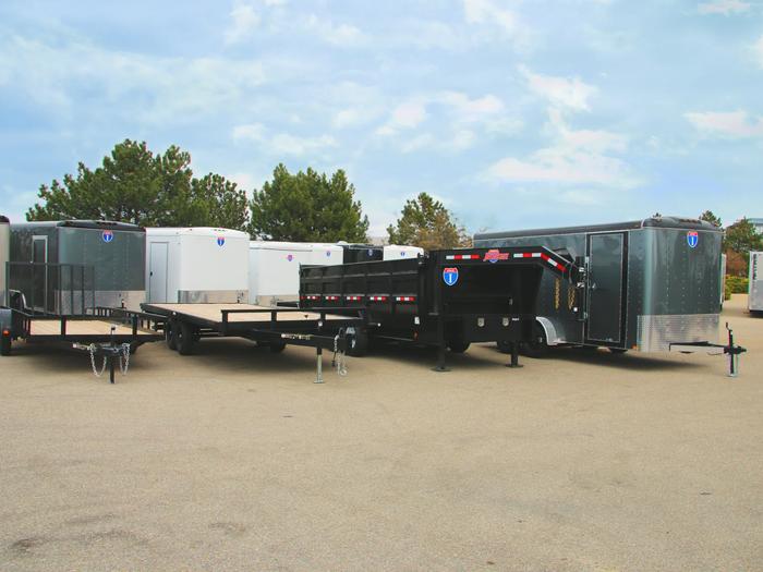 Lineup of a black utility, flatbed deckover, gooseneck dump, and silver enclosed cargo trailers parked together on a TrailersPlus dealer lot