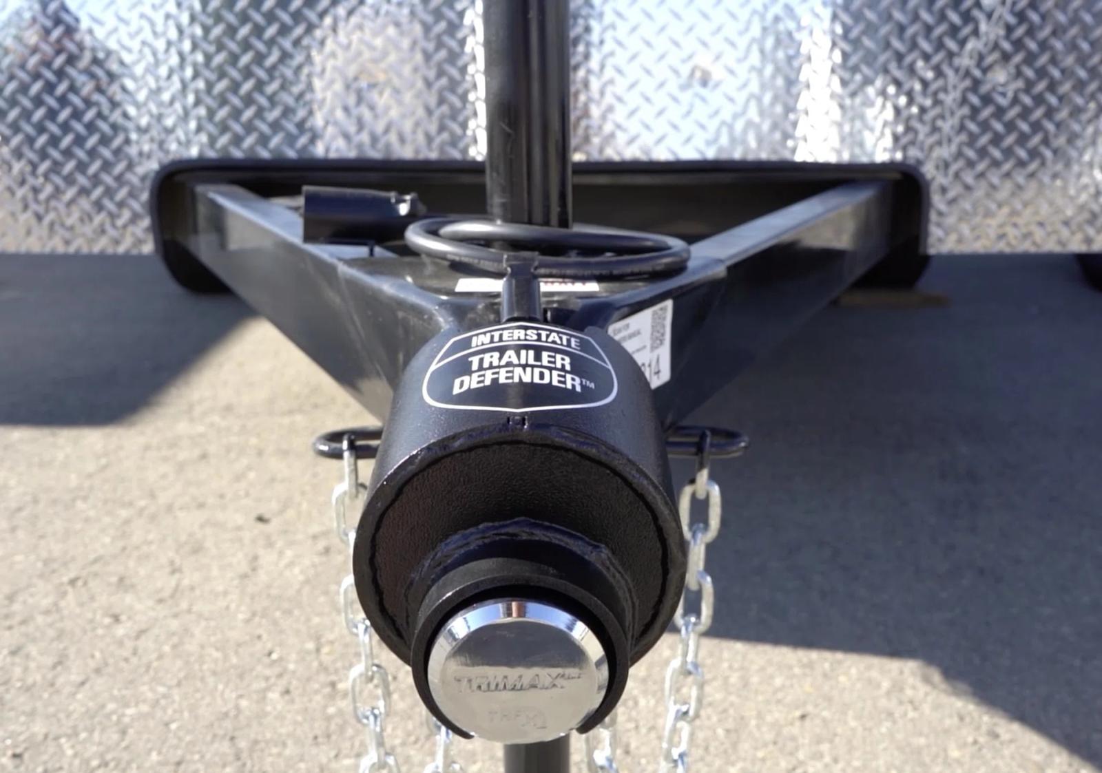 Close-up of a black trailer tongue with an Interstate Trailer Defender coupler lock and safety chains attached