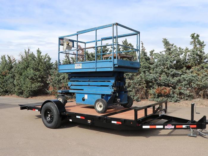 Blue scissor lift loaded onto a black tilt-deck equipment trailer with wood floor, parked at a sunny dealer lot